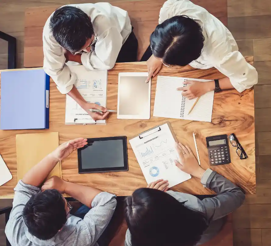 Four colleagues reviewing business reports, notes and a tablet around a wooden table.