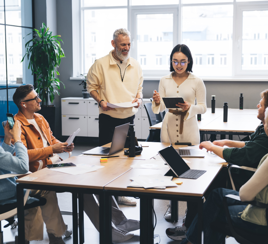 A team of colleagues discussing documents and a tablet around a conference table in a bright office.